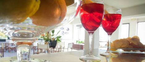 A bar area with two glasses of red beverage, a fruit bowl, and a plate with pastries.