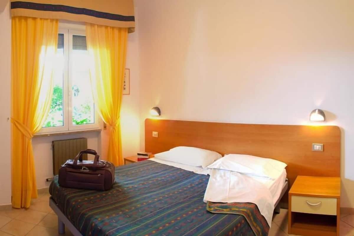 A hotel room with a bed, a bedside table, a lamp, and curtains.