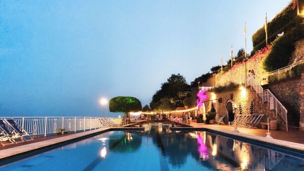 A swimming pool with a stone wall and stairs on one side, and a railing on the other. - Residence Sant'Anna (Pietra Ligure)