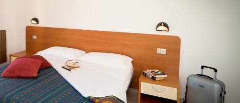 A hotel room with a wooden bed, a nightstand with a lamp, a drawer, and a suitcase.