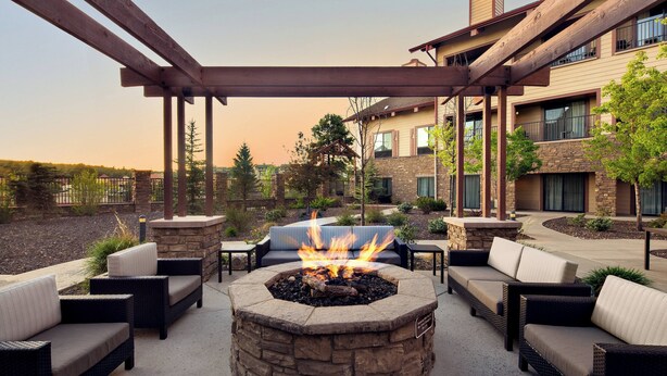 Un espacio al aire libre con una chimenea de piedra y mobiliario de mimbre bajo una pérgola de madera.