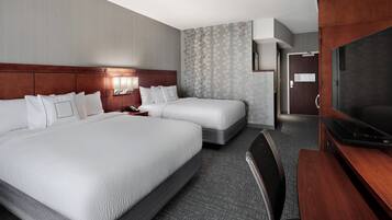 A hotel room with two beds, a desk, a TV, and a bathroom door.