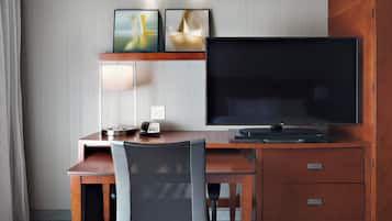 A hotel room with a wooden desk, a flat-screen TV, a lamp, and a telephone.