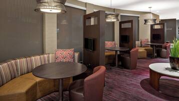 Um hall de hotel moderno com um sofá curvo, mesas redondas e luminárias contemporâneas.