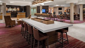 Un área de bar moderna con una barra alargada, varios taburetes y una llamativa pieza central de madera.