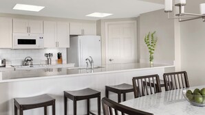Een moderne keuken met witte kasten, een centraal kookeiland met barstoelen, en een eettafel.