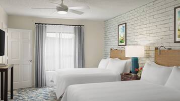 A hotel room with two beds, a ceiling fan, a white brick wall, and a window with curtains.