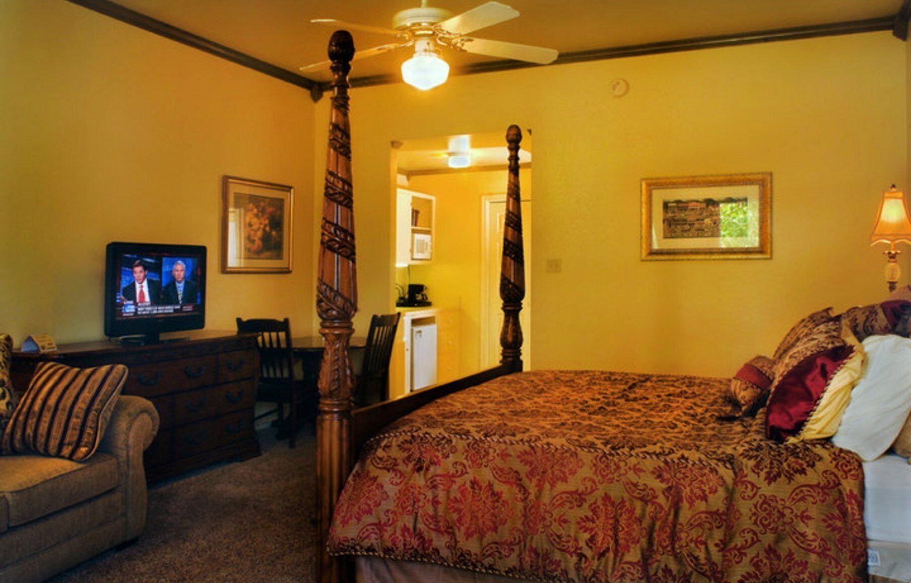 A bedroom with a four-poster bed, a television on a dresser, and a chair.