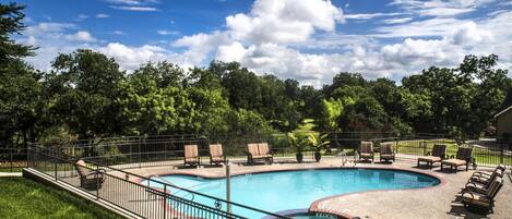 A swimming pool with lounge chairs and a fenced area, surrounded by trees and a clear sky.