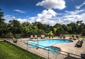 A swimming pool with lounge chairs and a fenced area, surrounded by trees and a clear sky.
