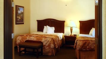 A hotel room with two beds, a ceiling fan, a bedside table with a lamp, and a small bench.