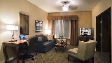 Une chambre d’hôtel équipée d’un bureau, d’un ordinateur portable, d’une chaise, d’un canapé et d’une télévision.