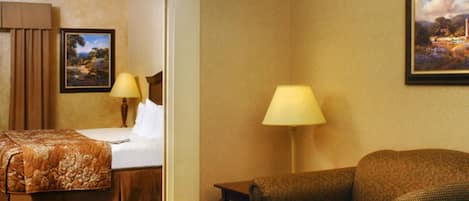 A hotel room with a bed, a sofa, a desk, two lamps, and a painting on the wall.