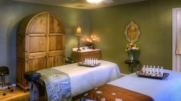 Een kamer met twee bedden, een houten garderobe, een bureau met een lamp en een plafondventilator.