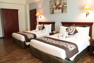 Habitación de hotel con dos camas, suelo de madera, un cuadro en la pared y una lámpara en la mesita de noche.