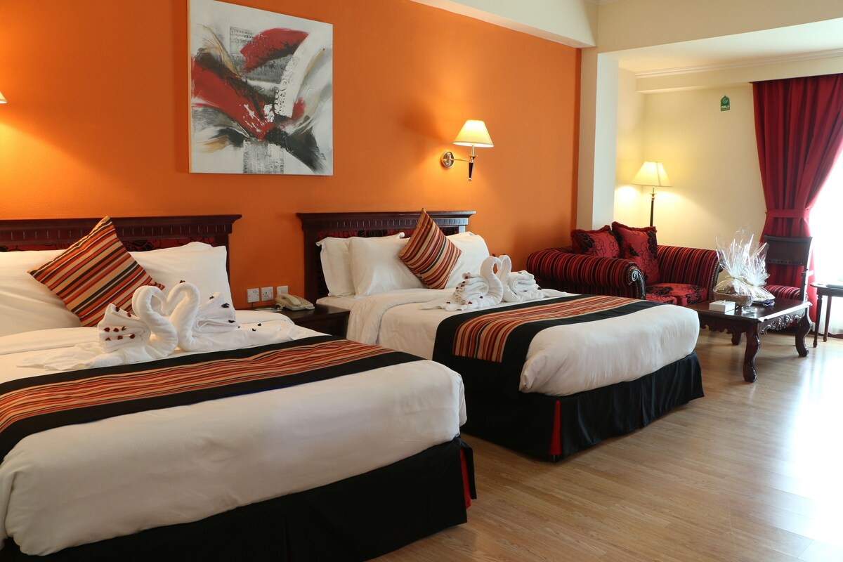 A hotel room with two beds, a painting on the wall, and a red curtain.