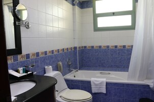 Un baño con bañera, inodoro, lavamanos y una ventana con cortina.