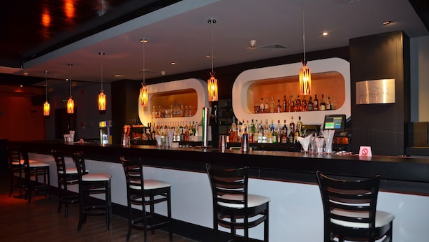 Eine Bar mit einer Theke, mehreren Sitzplätzen und hängenden Pendelleuchten.