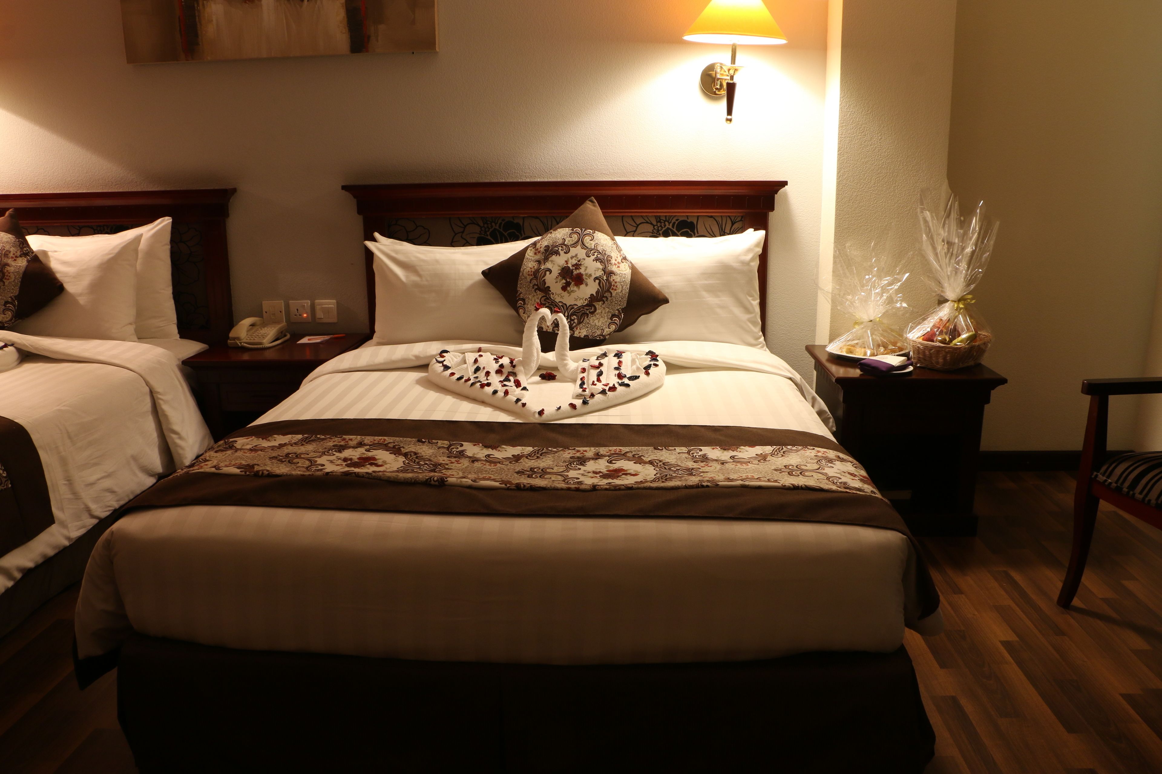 Une chambre d’hôtel avec deux lits, chacun doté d’une tête de lit en bois, d’une table de chevet avec une lampe et d’un coussin décoratif.