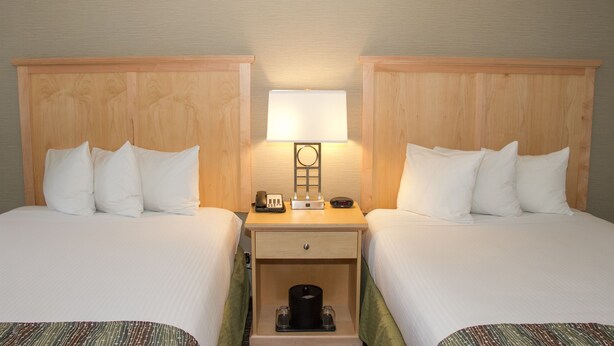 A hotel room with two beds, a nightstand with a lamp, a phone, and a small drawer.