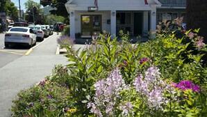 A motel named Villager with a vacancy sign, a porch with chairs, and a garden with flowers in front.
