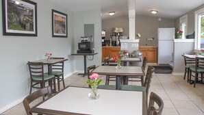 A dining area with a table and chairs, a kitchen in the background, and framed pictures on the wall.