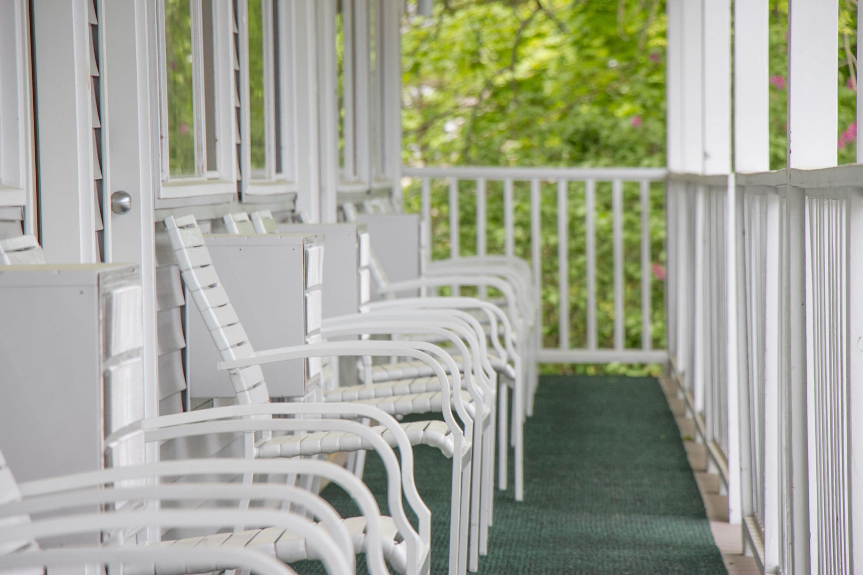 A row of white metal chairs with a green carpeted floor and white railings.