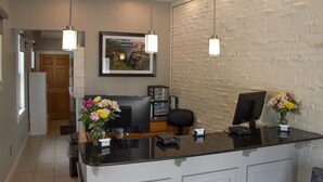 A reception desk with two computer monitors, a vase with flowers, and a framed picture on the wall.