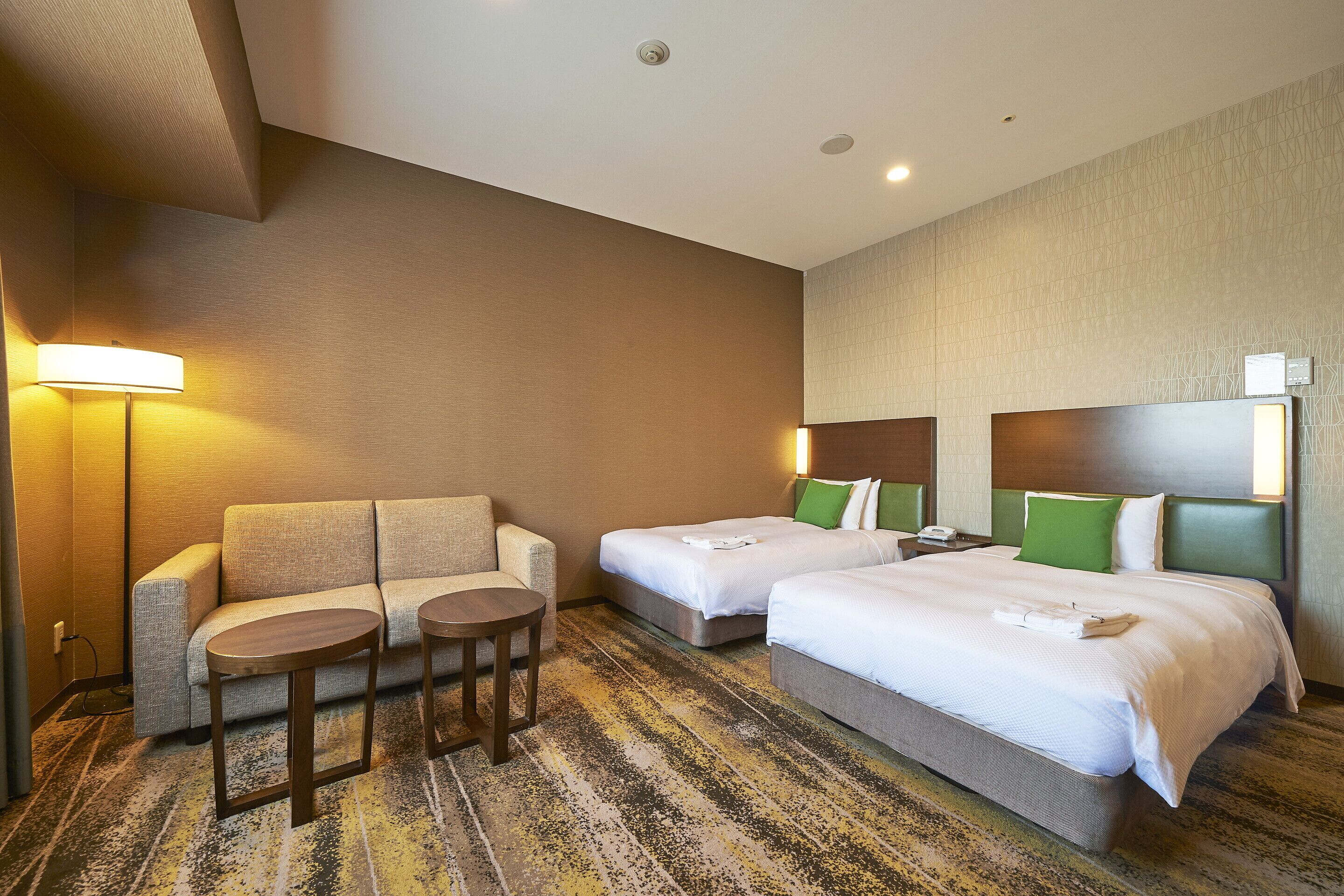 Une chambre d’hôtel avec deux lits, un canapé, une petite table et une lampe.
