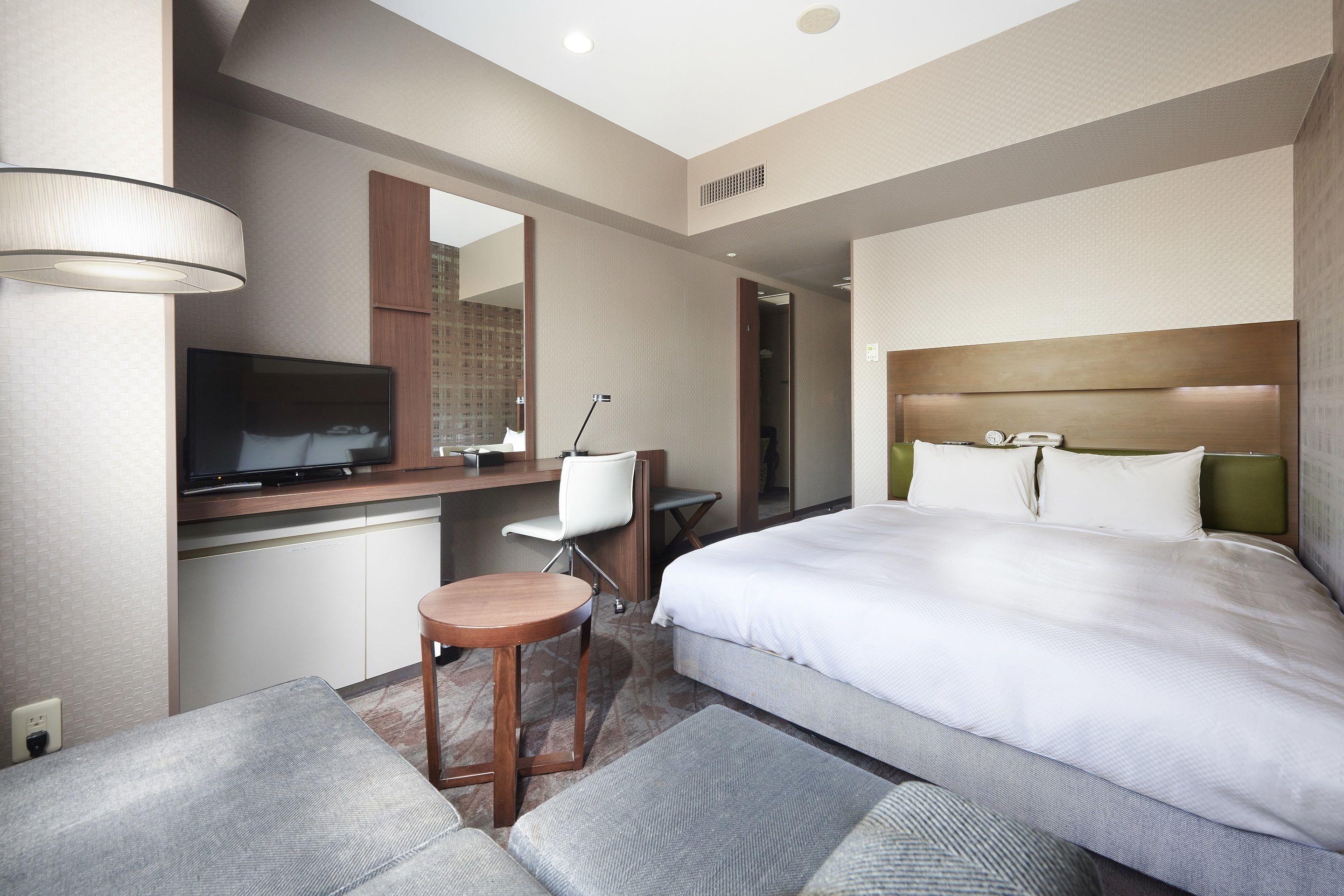 A hotel room with a bed, a desk with a chair, a television, and a mirror.