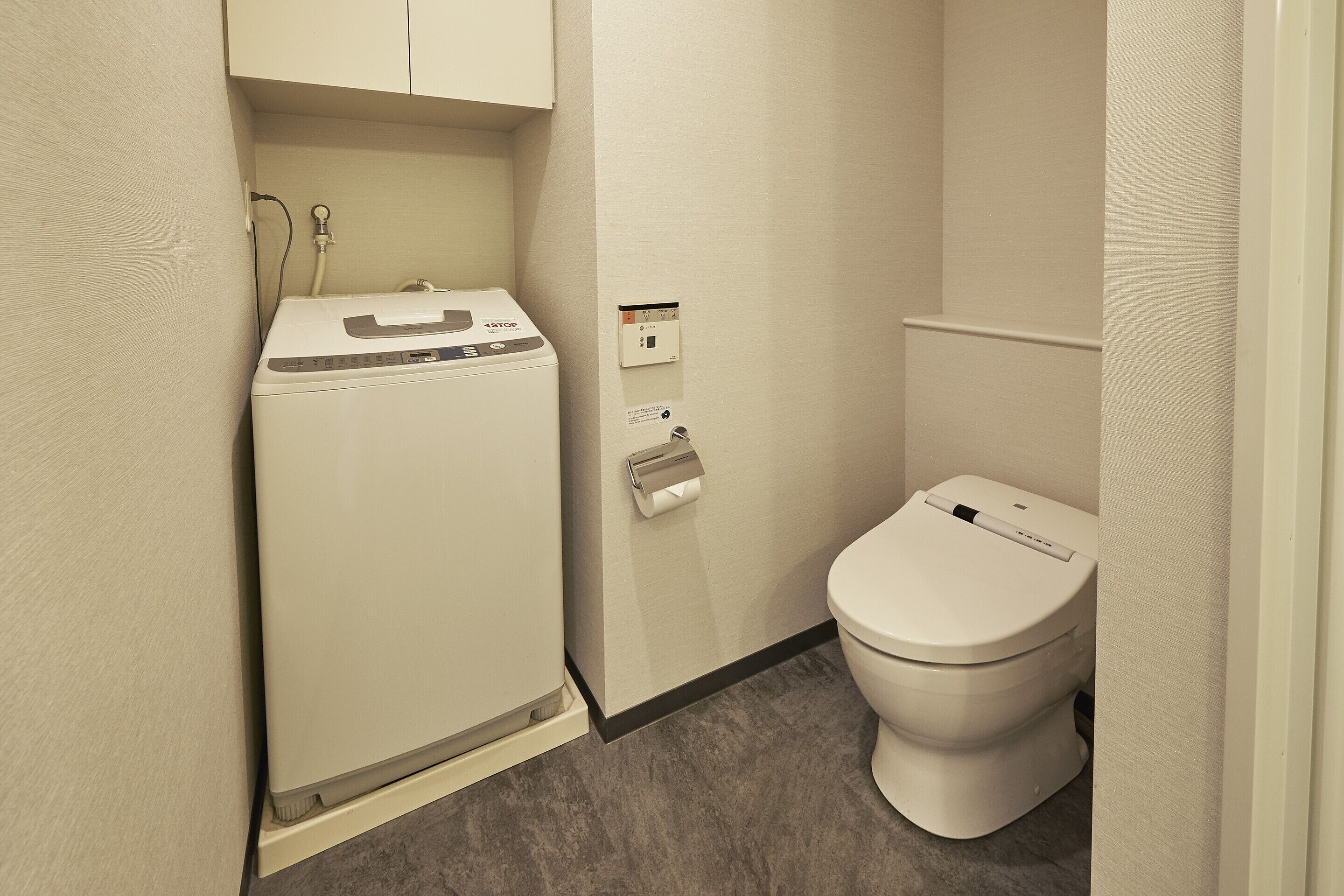 Baño pequeño con lavadora, inodoro y dispensador de toallas.