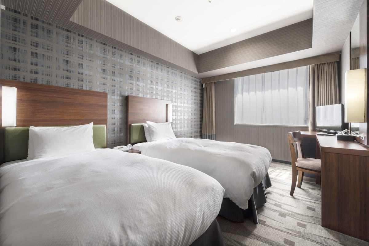 A hotel room with two beds, a desk, and a chair.