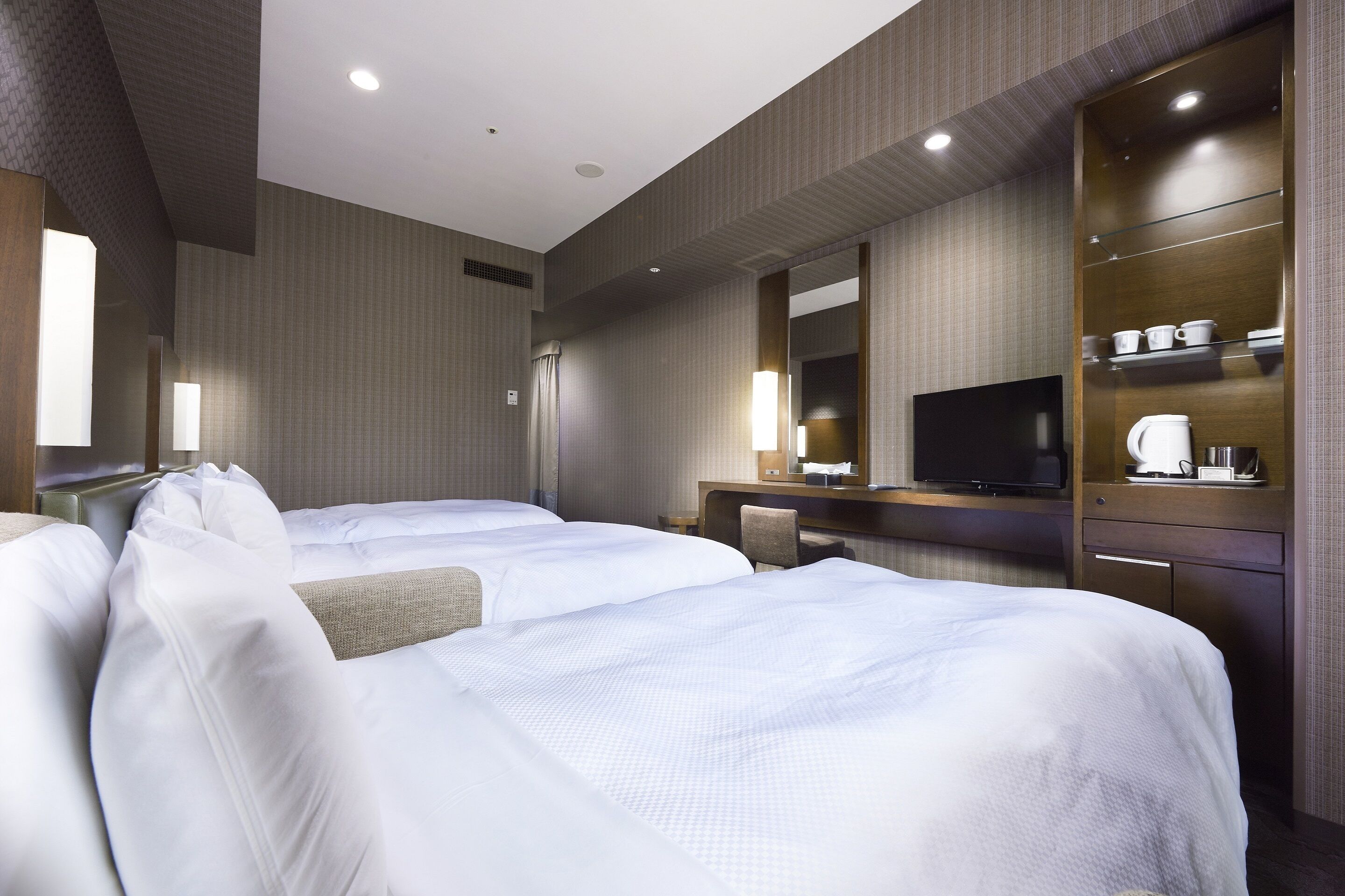 Quarto de hotel com duas camas, uma televisão, uma escrivaninha com cafeteira e um espelho.