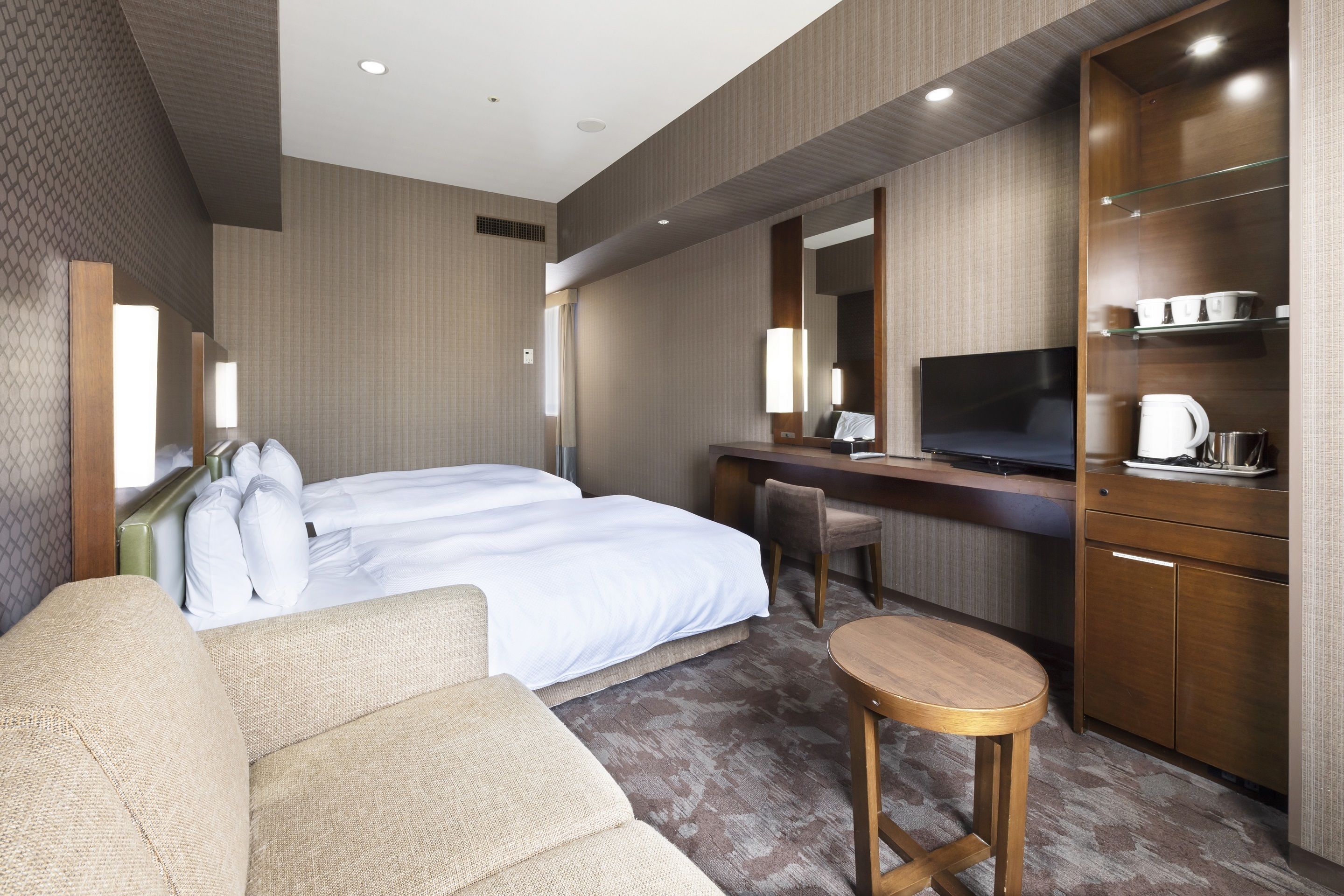 A hotel room with a bed, a desk, a TV, and a seating area.