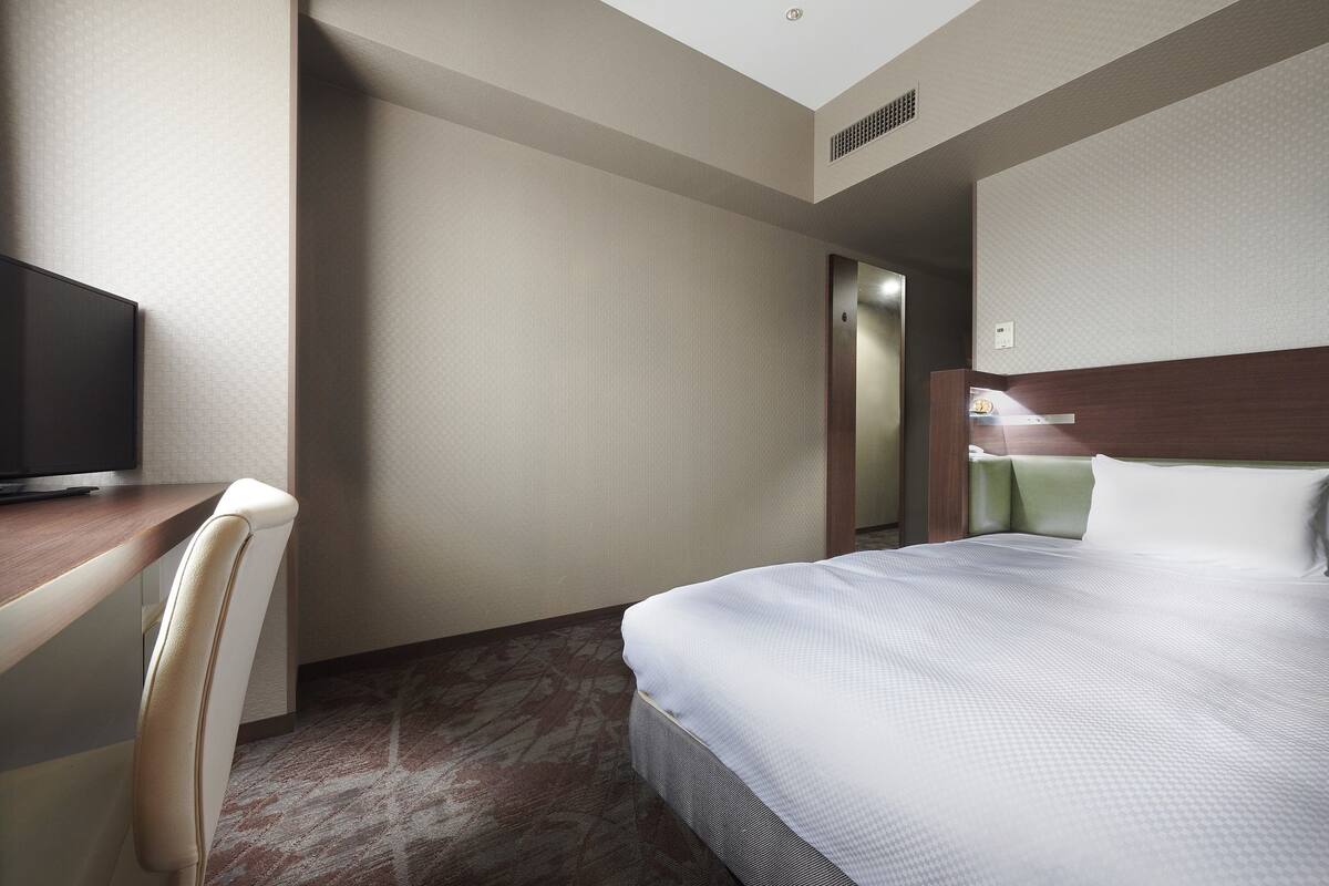 A hotel room with a bed, a desk, and a television.