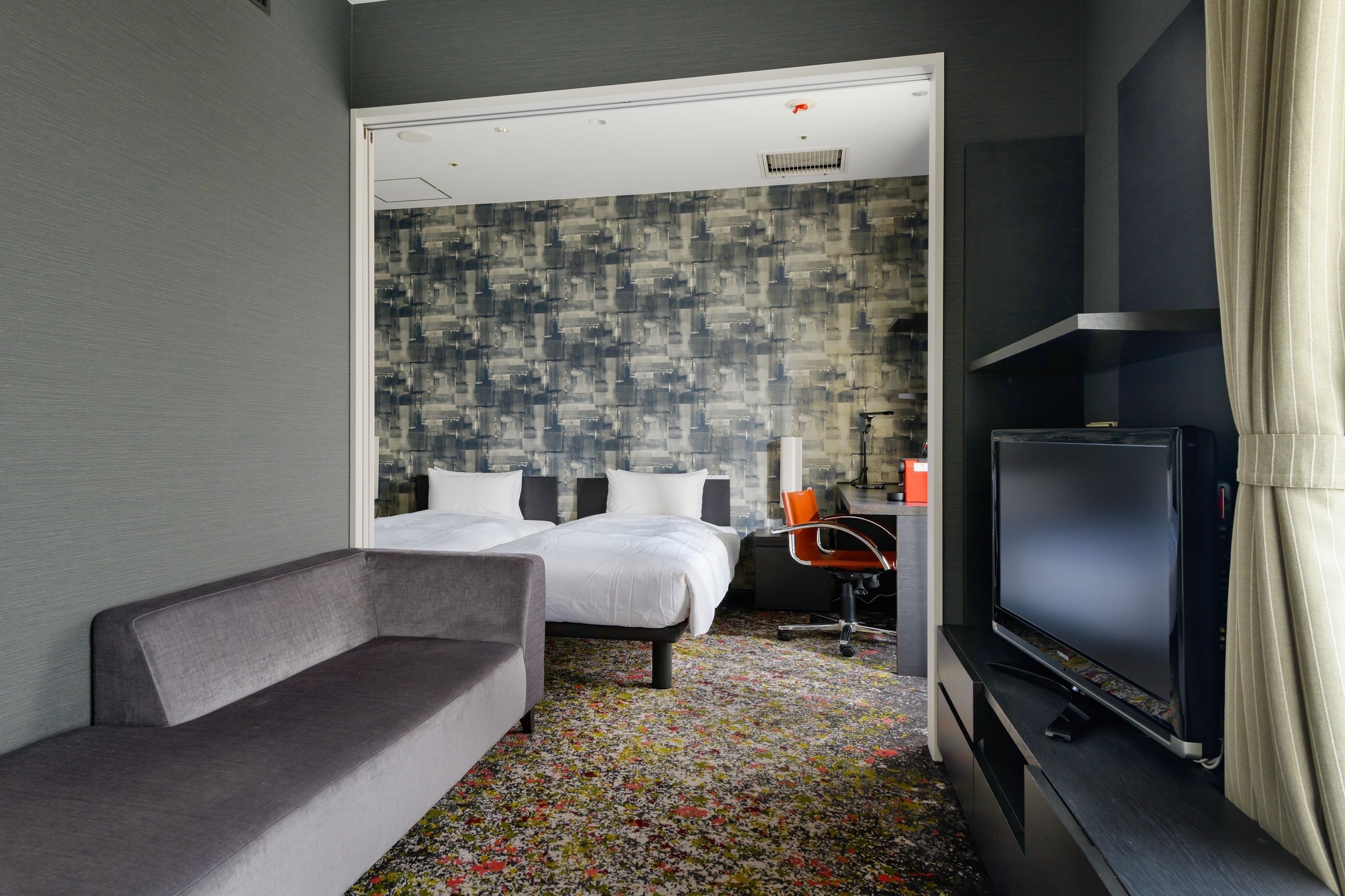 A modern hotel room with a bed, a sofa, a TV, and a desk with a chair.