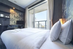 A hotel room with a large bed, a flat-screen TV, a desk with a chair, and a view of the city through the window.