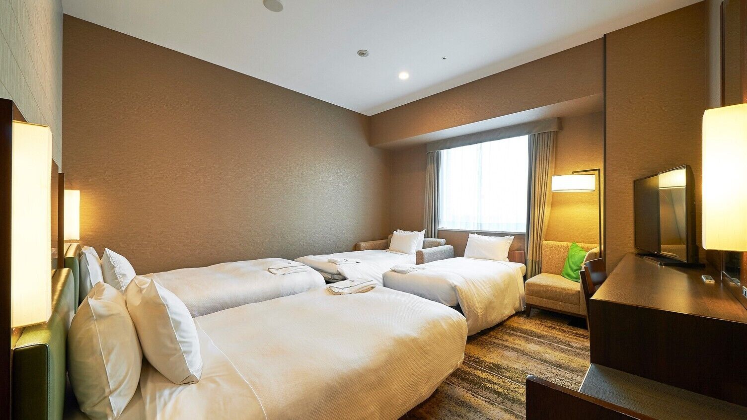 A hotel room with two beds, a desk, a chair, a TV, and a window with curtains.