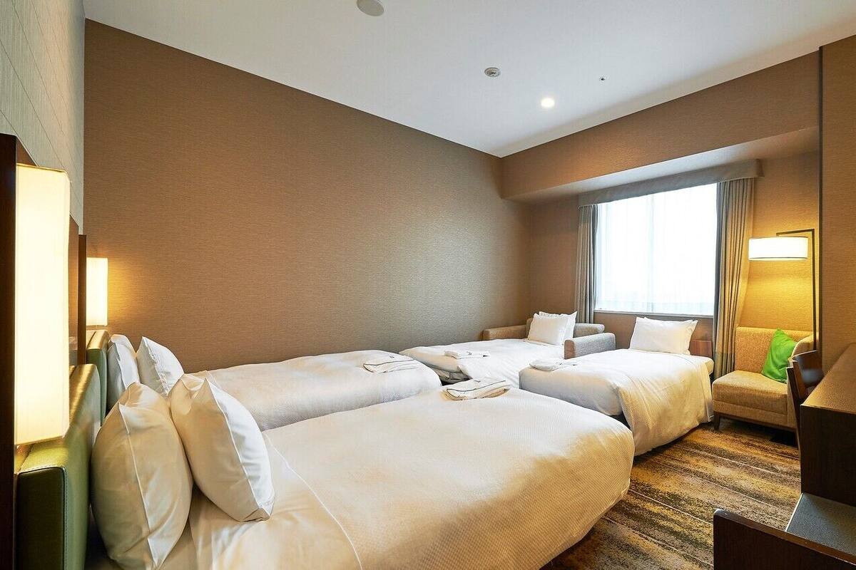 A hotel room with two beds, a desk, a chair, a TV, and a window with curtains.