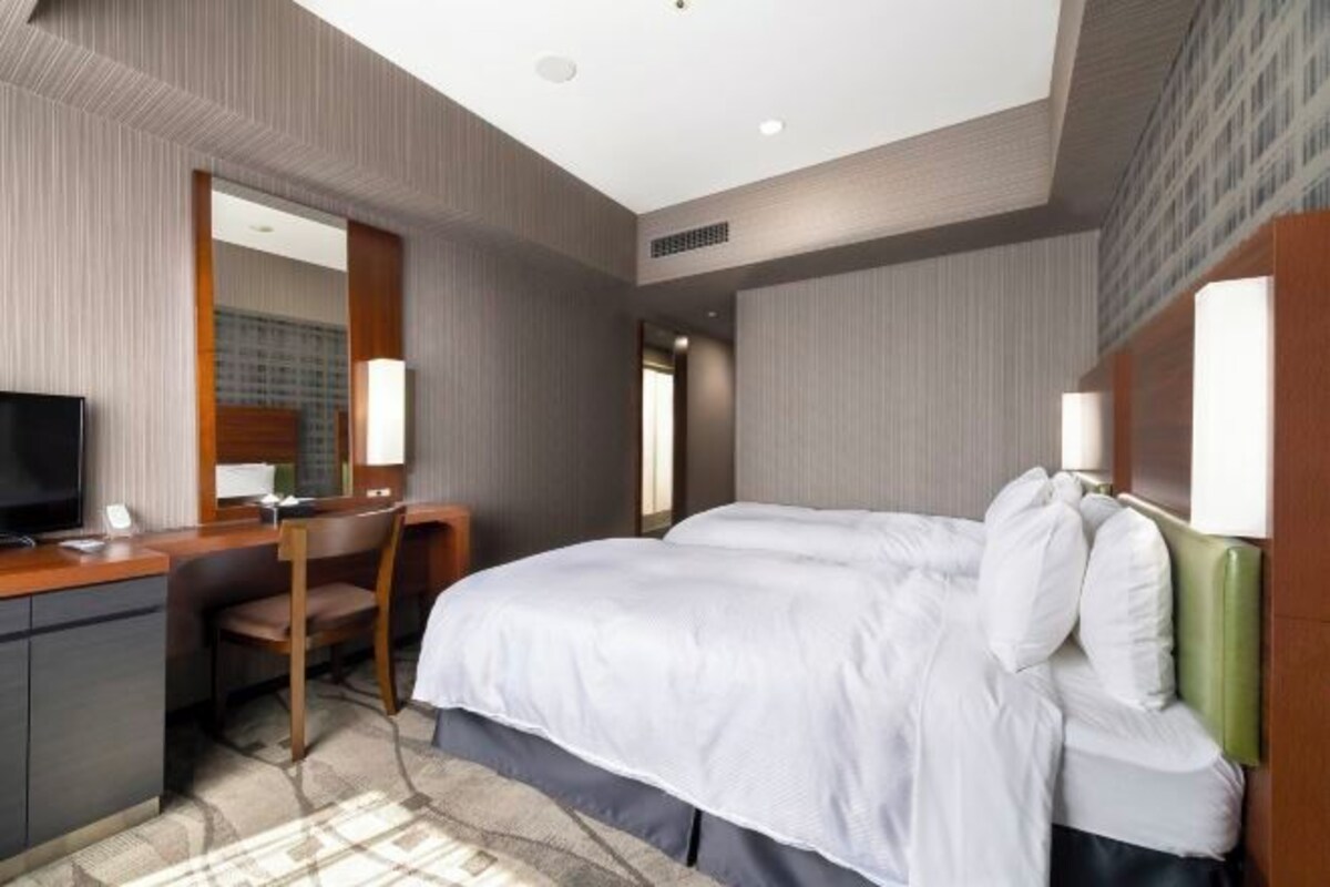 A hotel room with a bed, a desk, a chair, a television, and a mirror.