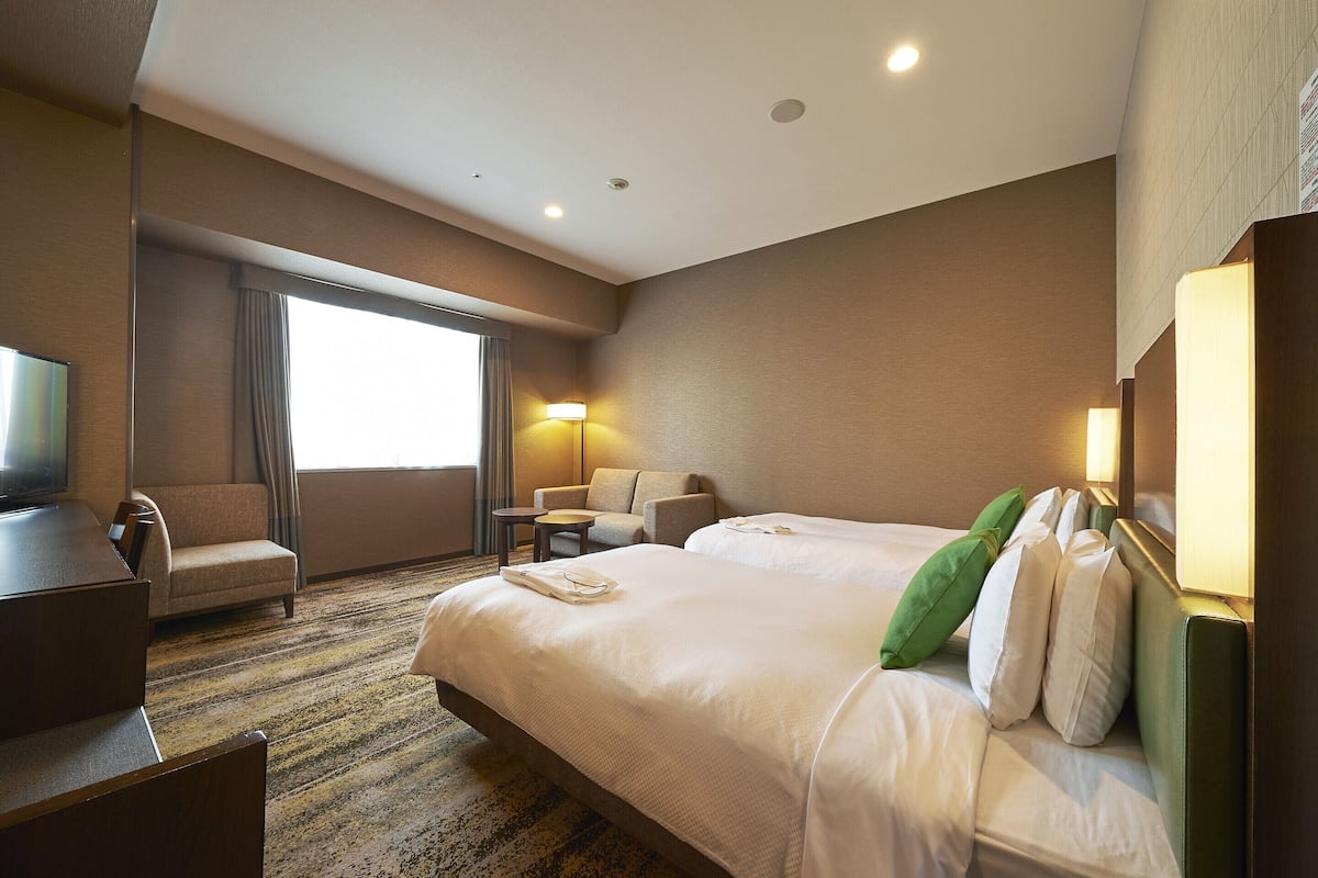 A hotel room with two beds, a desk, a chair, a TV, and a window with curtains.