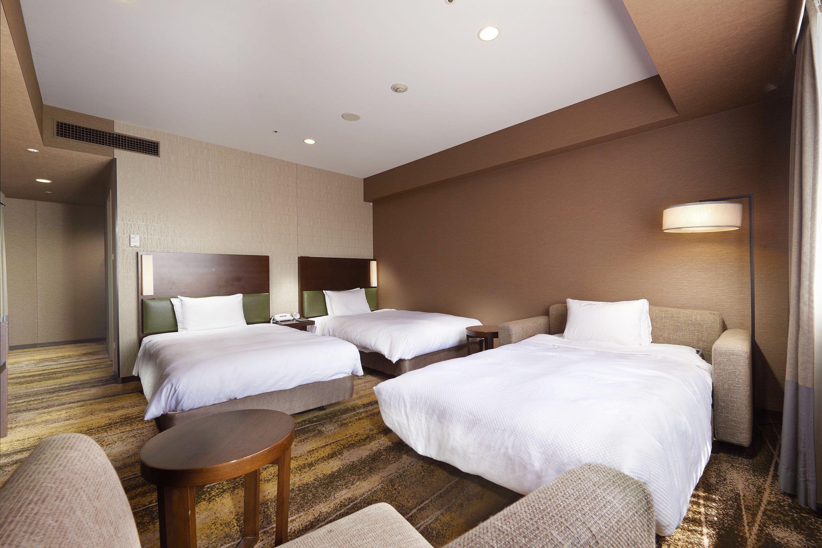 Habitación de hotel con dos camas, un sofá, una mesita y una lámpara.