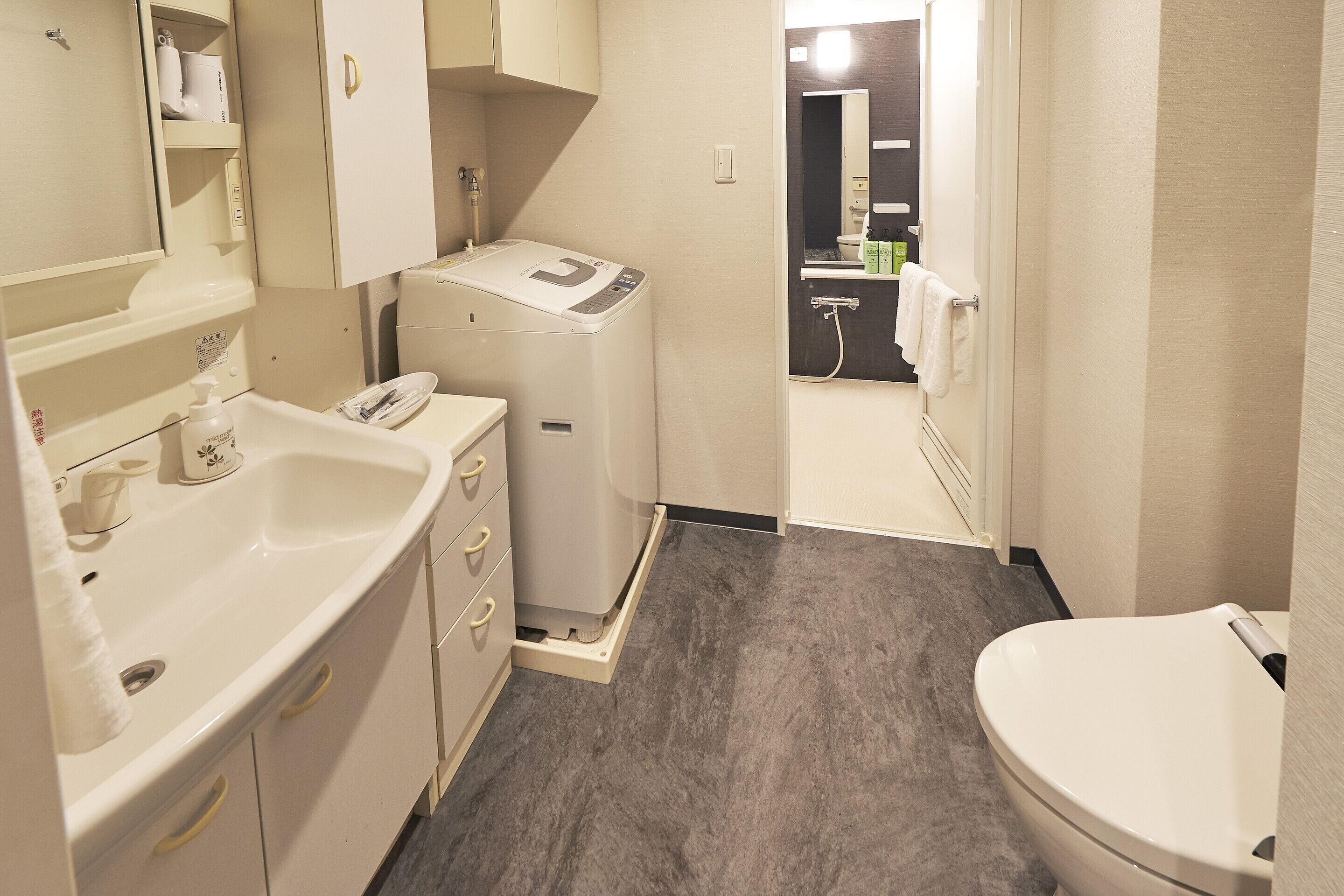 A compact bathroom with a sink, toilet, and a compact washing machine.