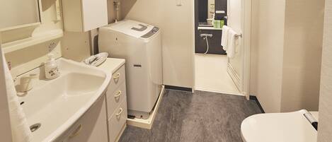 A compact bathroom with a sink, toilet, and a compact washing machine.