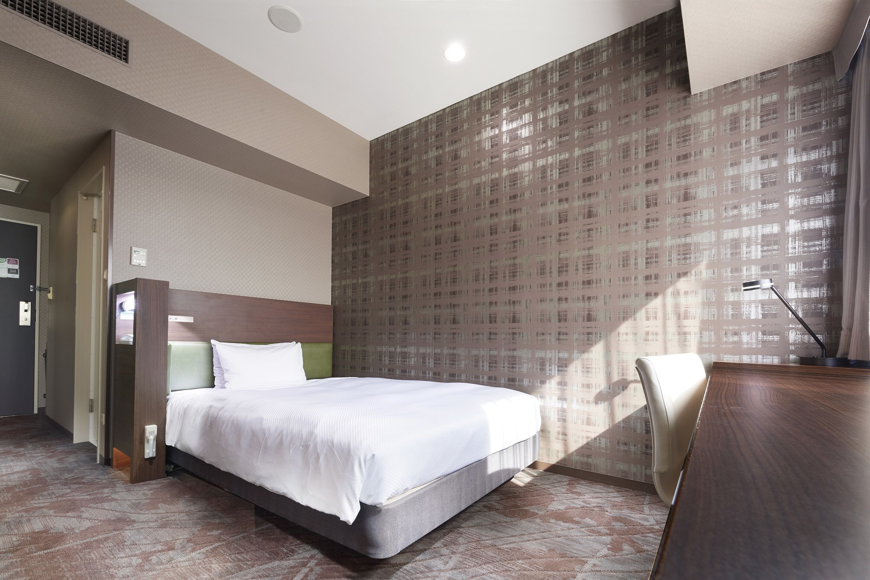 Een hotelkamer met een bed, een bureau en een stoel. Er is een raam met gordijnen en een deur.