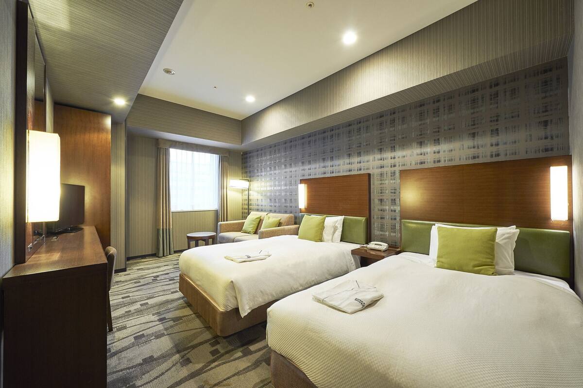 A hotel room with two beds, a desk, and a chair.