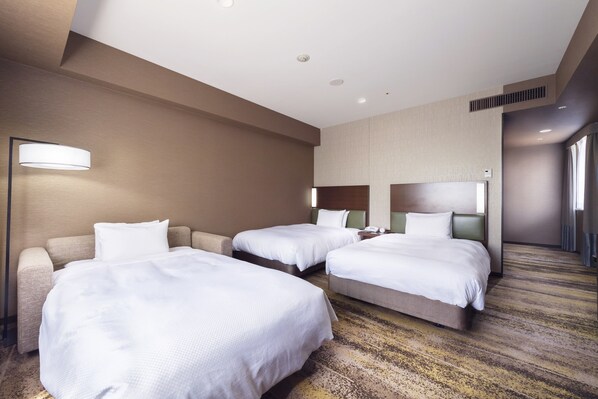 A hotel room with two beds, a sofa, and a lamp.