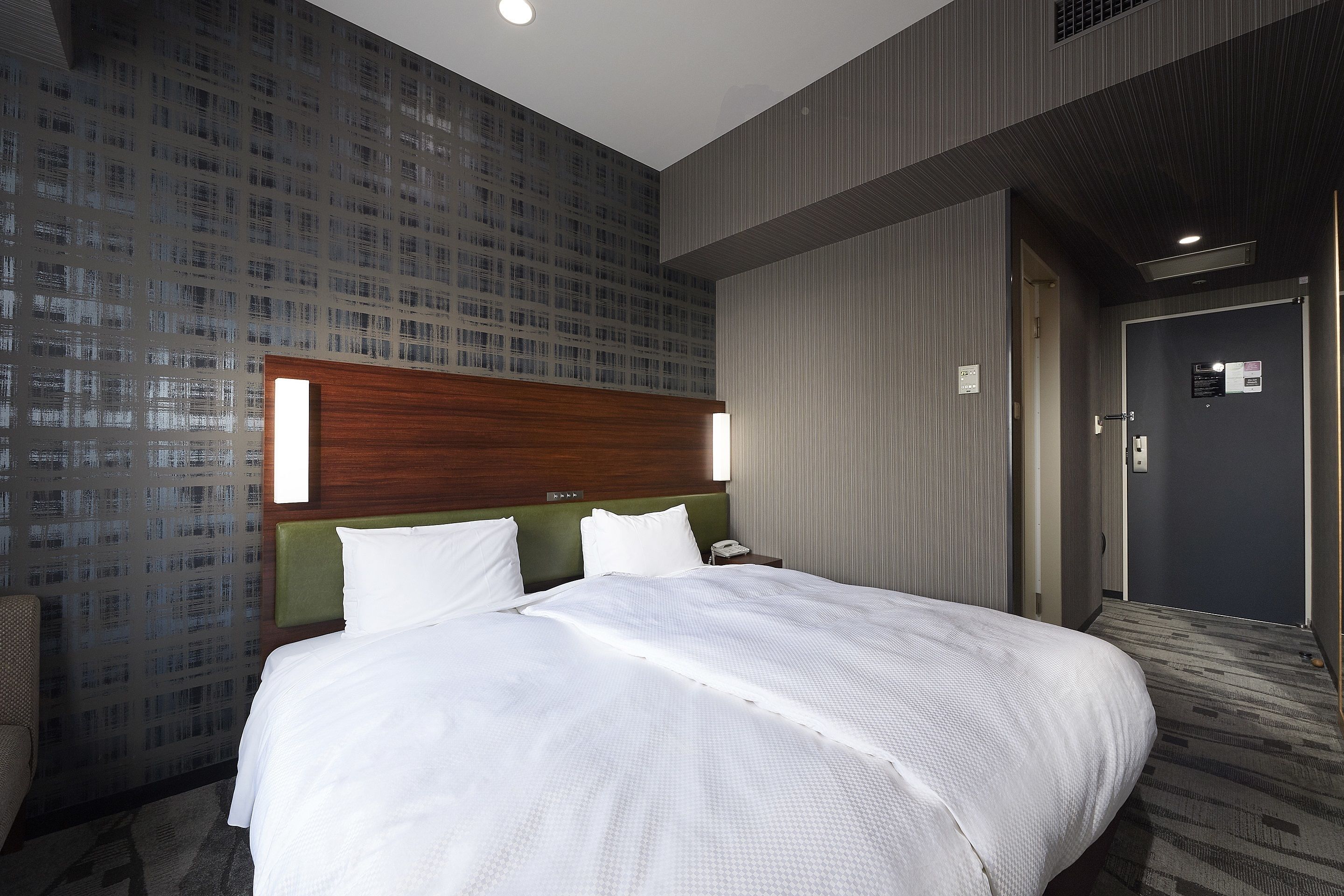 A hotel room with a large bed, a wooden headboard, a green accent wall, and a patterned wallpaper.