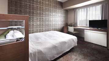 A hotel room with a bed, desk, TV, and a window with curtains.