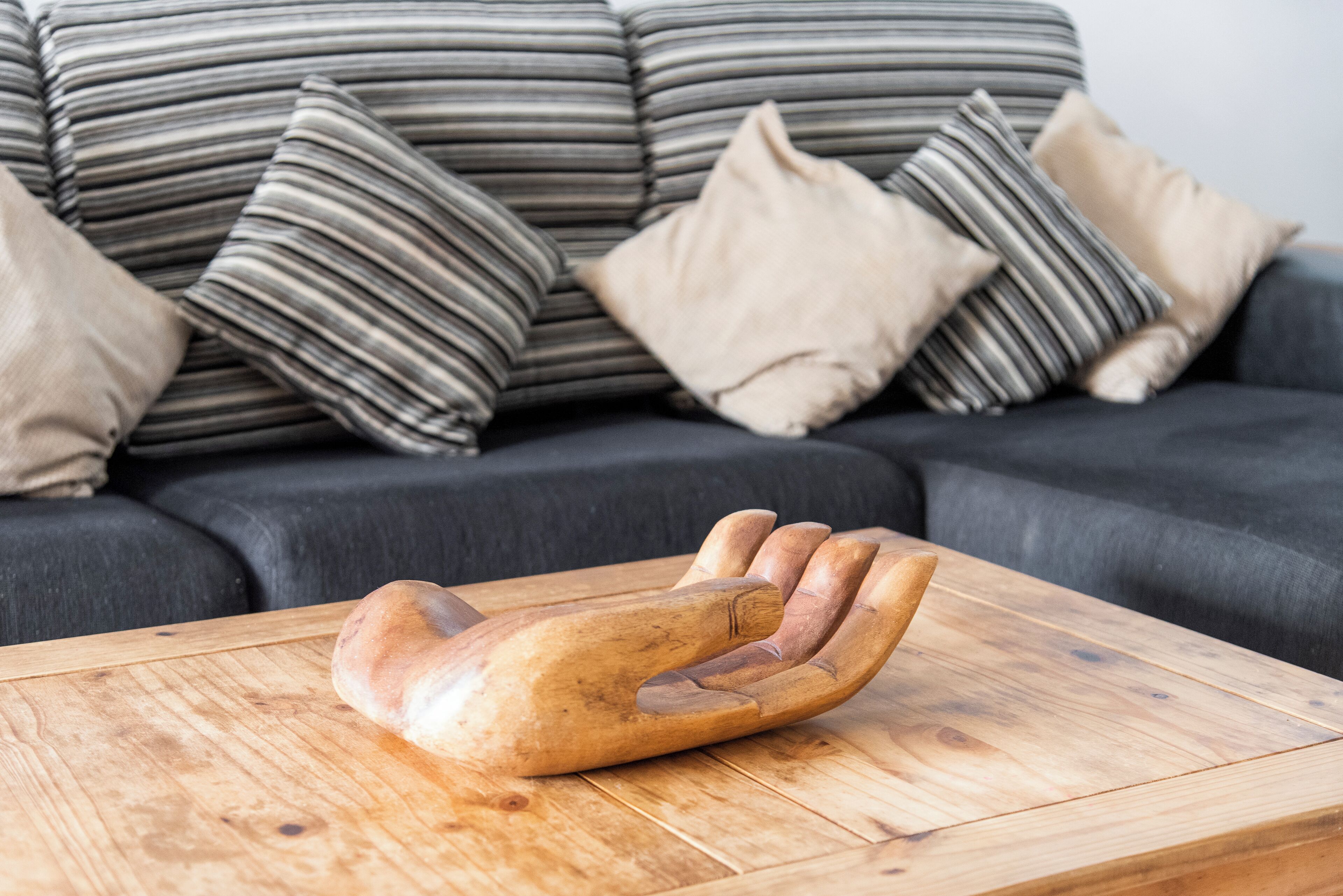 A wooden hand-shaped object on a wooden table in a living room with a dark sofa and striped cushions.